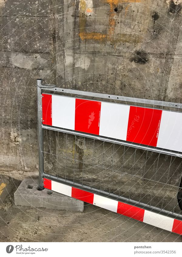 A red-white striped barrier leans against a concrete wall cordon Control barrier Warn interdiction Stripe Reddish white Wall (building) Grating Dirty
