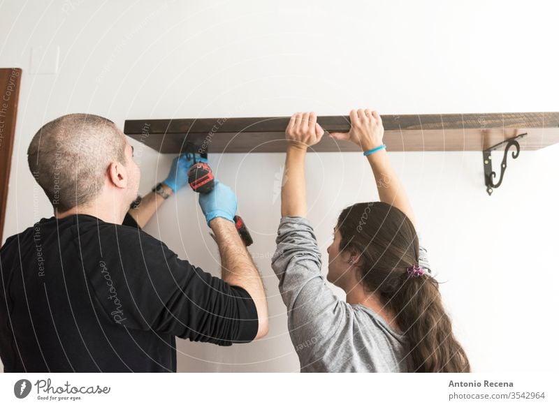 man with electric screwdriver places bookshelf on a wall with the help of his wife's handyman bald beard beginnings casual caucasian change construction