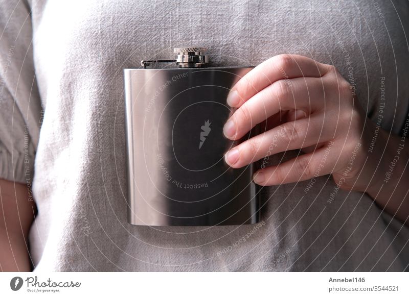 Hand holding a stainless steel flask for liqueur, alcohol and beverage concepts in close-up background alcoholic Drinking Design by hand booze Party Steel Water