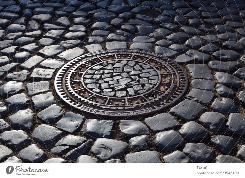Manhole cover in the cobblestone pavement at evening light Old town Street Cobblestones Drainage system cobbled street Paving stone manhole cover Gully