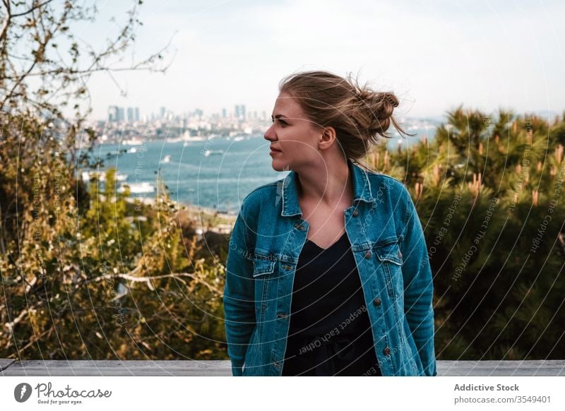 Young woman standing against green plants and sea view seashore palace garden terrace tourist tree travel istanbul turkey sky enjoy cloudy jeans jacket female