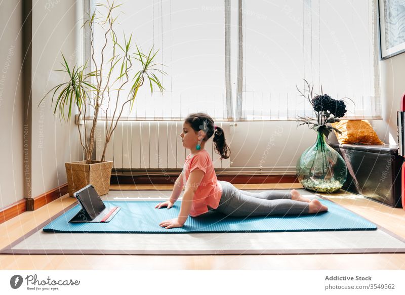 Fotografia do Stock: Little girl doing stretching exercises, practicing yoga  on fitness mat at home