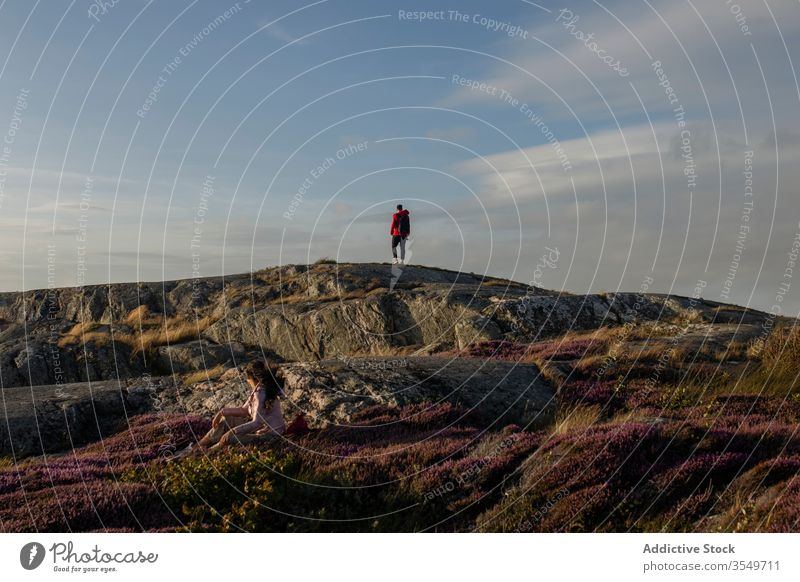 Anonymous couple of travelers hiking on rocky cliff landscape nature grass picturesque tourism walk vacation relationship together adventure admire journey trip