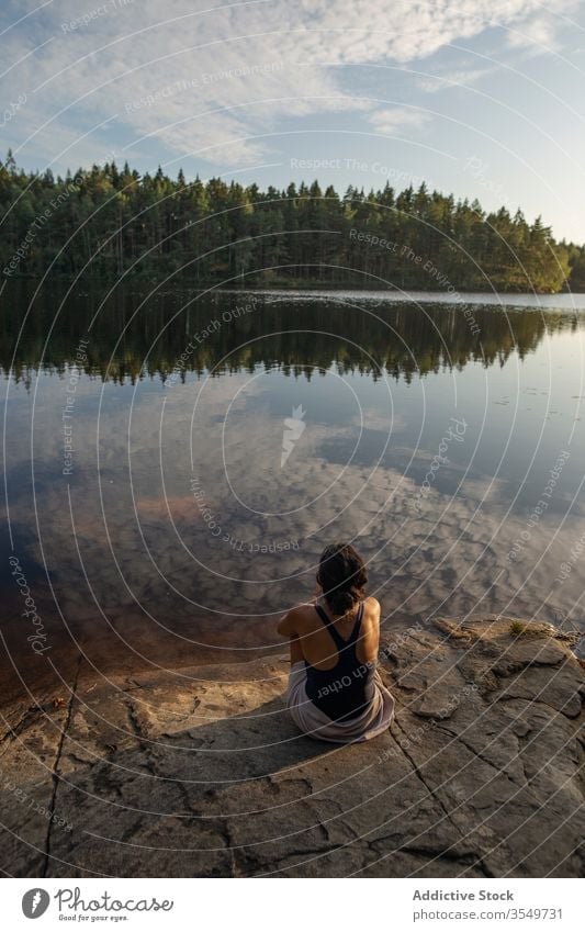 Woman in swimsuit sitting on lake shore in summer woman enjoy landscape rocky coast forest female majestic tranquil calm serene harmony peaceful idyllic wood