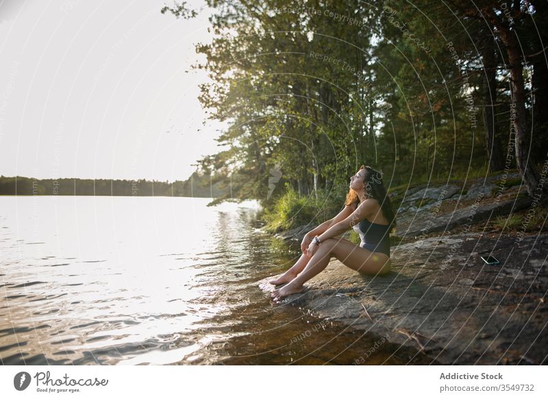 Woman in swimsuit sitting on lake shore in summer woman enjoy landscape rocky coast forest female majestic tranquil calm serene harmony peaceful idyllic wood