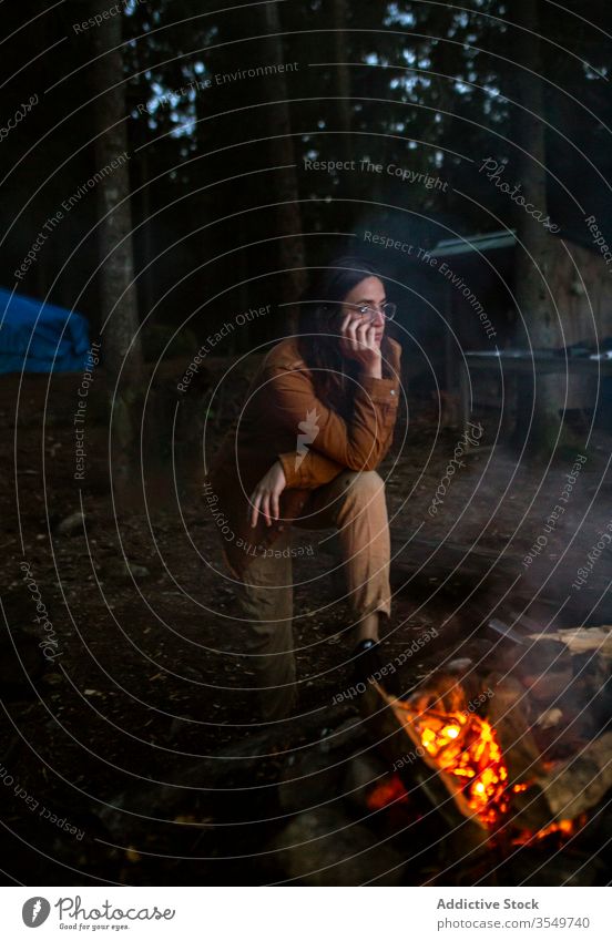 Pensive traveling woman warming up near bonfire in woods pensive camper warm up campfire relax ponder evening female firewood forest log calm traveler tranquil