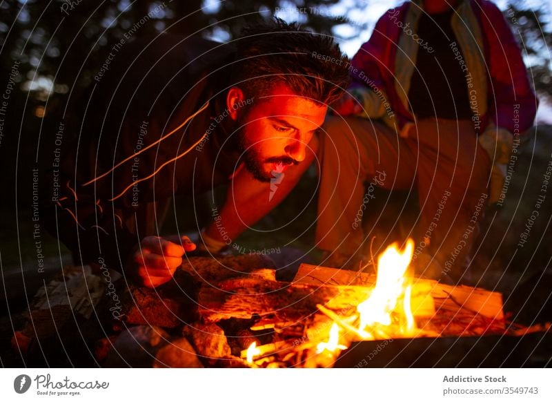 Man with firewood making campfire in forest man camper bonfire night log warm up male calm traveler tranquil woods enjoy weekend evening trees relax nature