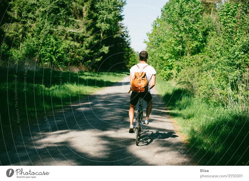 A cyclist on a path through the forest on a bike trip Bicycle Man Trip Nature Cycling tour Summer sunny Backpack T-shirt Dark-haired trees off Spring