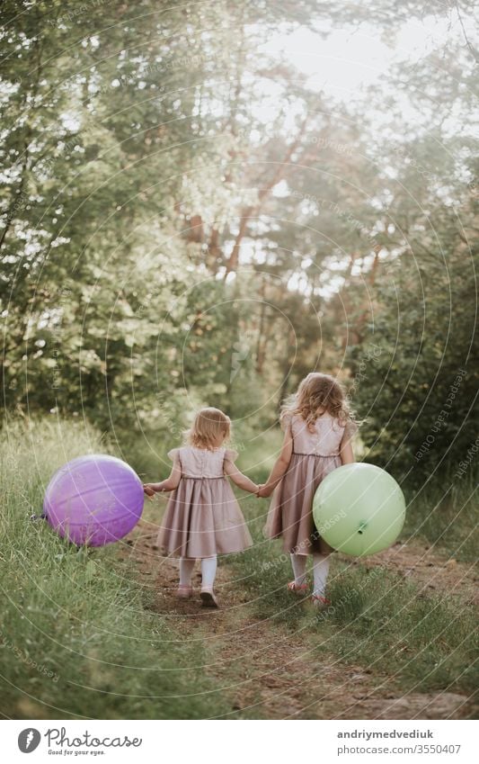 two beautiful little girls in the summer in a park with balloons in hands. Happy girl with balloons. kids children freedom family happy playing holding running