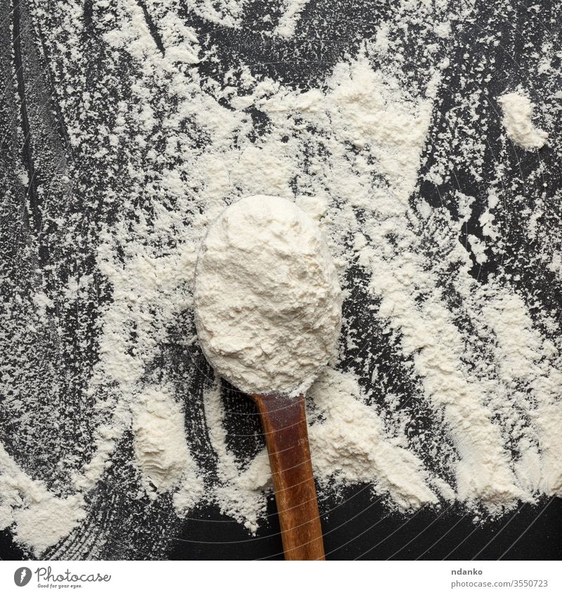 white wheat flour in a wooden brown spoon, black background table board backdrop cereal closeup cooking cuisine culinary dry food fresh heap ingredient kitchen