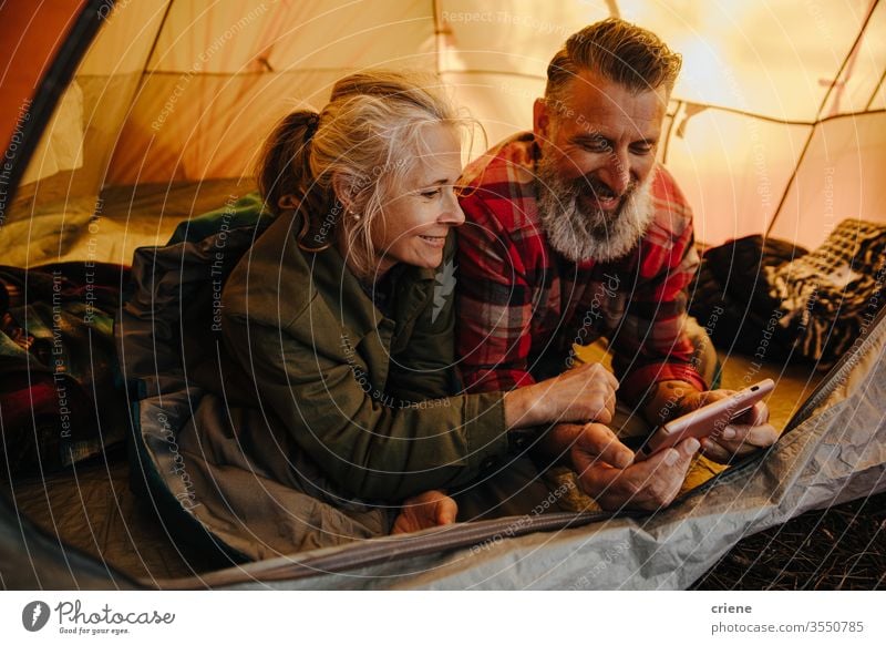 Happy senior couple using phone inside tent on camping trip smartphone technology smile connected internet browsing online happy enjoying active activity