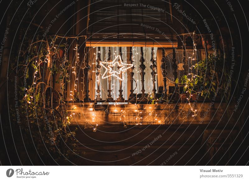 A light star hanging on a balcony decorated with light garlands at night illuminate branch shine tree house evening dark holiday festive glow celebrate