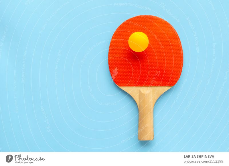 Red racket for table tennis with yellow ball on blue background. Ping pong sports equipment in minimal style. Flat lay, top view, copy space ping handle game