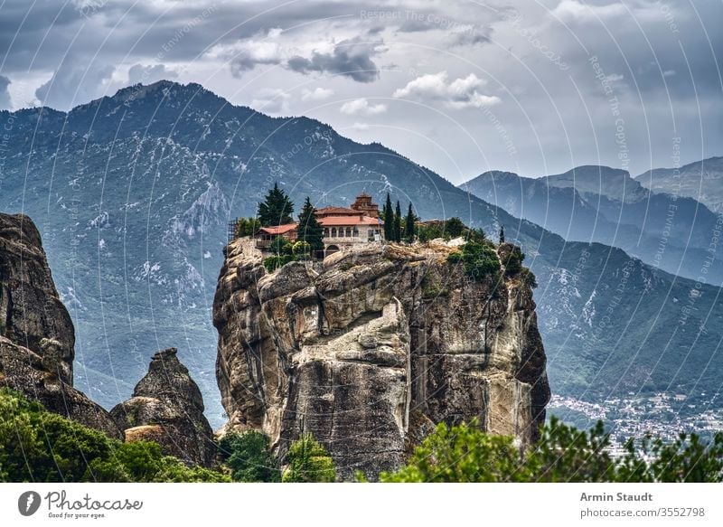 Monastery on a huge rock in Meteora, Greece with mountain range and dramatic clouds meteora monastery abbey church cliff culture architecture attraction