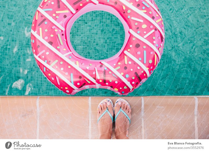 top view of a woman feet flat lay. Woman relaxing in the pool with pink donuts in hot sunny day. Summer holiday idyllic. Enjoying suntan Woman in bikini on the inflatable in the swimming pool.