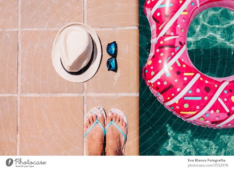 top view of a woman feet flat lay with hat and sunglasses. Woman relaxing in the pool with pink donuts in hot sunny day. Summer holiday idyllic. Holidays concept