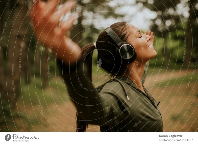 Young woman with earphones preading her arms in the forest because she enjoys training outside music female listening lifestyle caucasian happiness outdoor