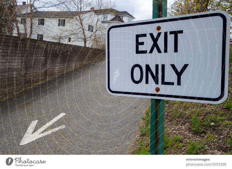 Suburban area with exiting driveway with painted arrow on tarmac and green pole black and white sign reading "Exit Only" reflective sign surface spring