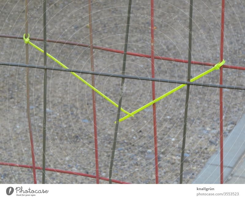Red and black construction fence standing one behind the other, two yellow cable ties attached to the red one, which are connected to each other Cable strap