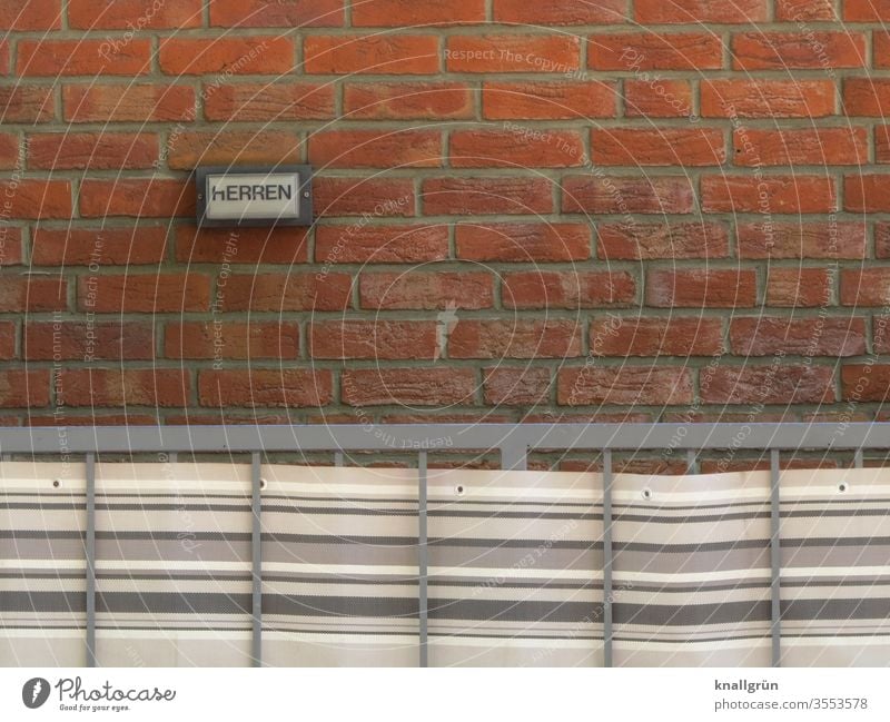 Small sign HERREN on red brick wall, in front of it a metal railing with striped awning fabric Signs and labeling Gentlemen's toilet Signage Exterior shot