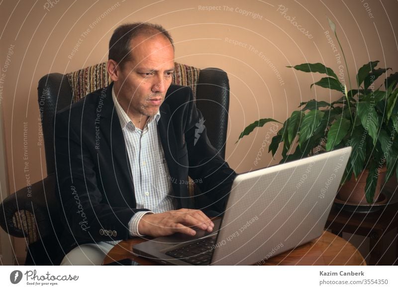 Senior adult male working from home using his laptop with plant on backgroung work from home senior man telework computer online social life isolation distance