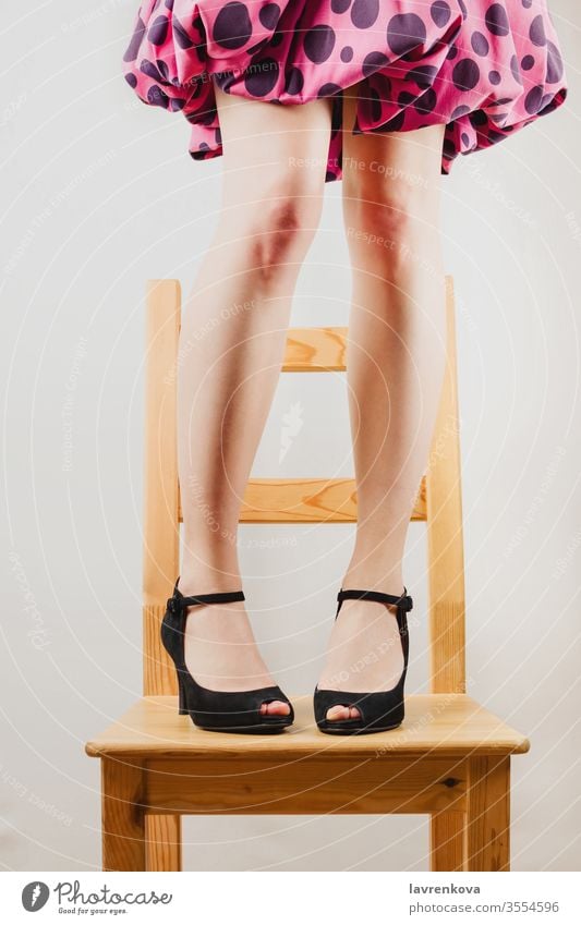 Selective shot of white woman's legs in black high heeled shoes standing on a wooden chair. dressed up fun body faceless toned people lady person attractive