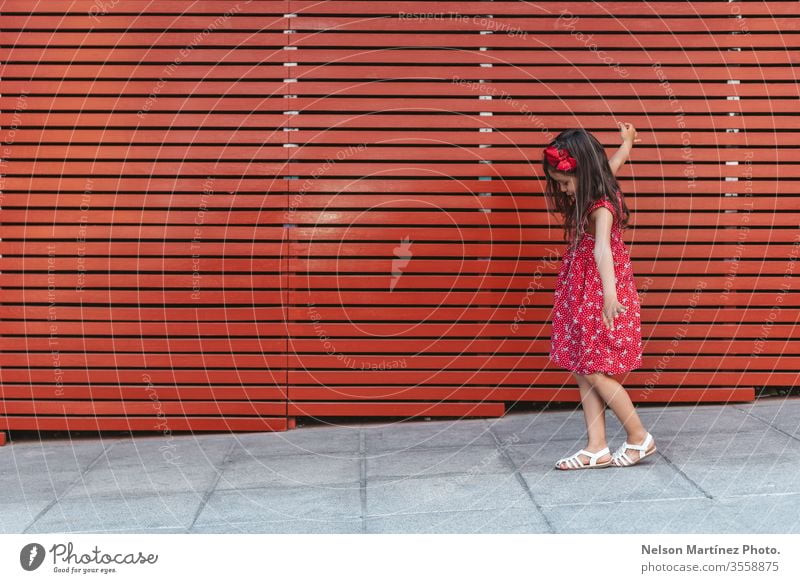 Happy little girl with arms wide open in front of a red background, wearing a red dress. summer fun cute kid funny happy hispanic childhood happiness portrait