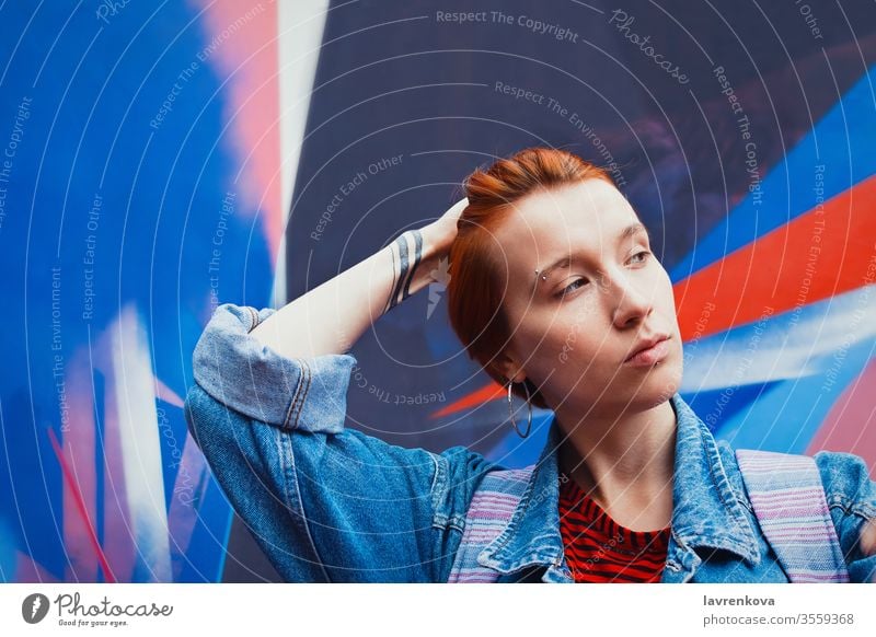 Young adult white woman in jeans jacket with died red hair flattens her hair down, lifestyle portrait with selective focus model street vacation female dyed