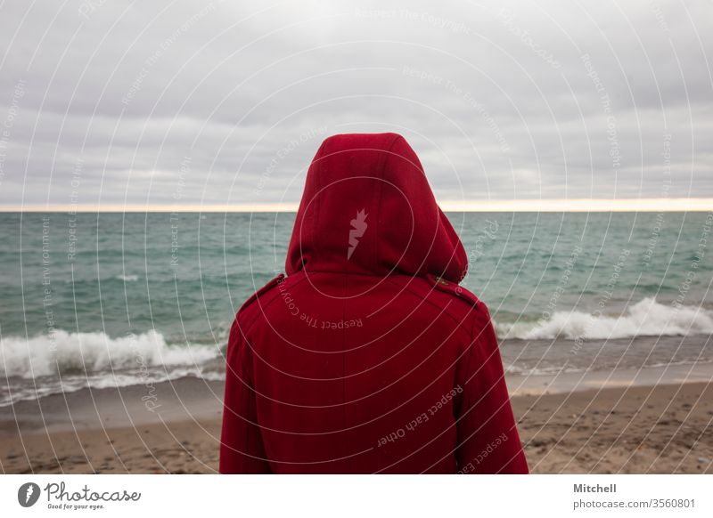 A Person in a Bright Red Jacket looks out to the Sea ocean view red coat jacket person looking longing wanderlust travel tourism vacation getaway waves water