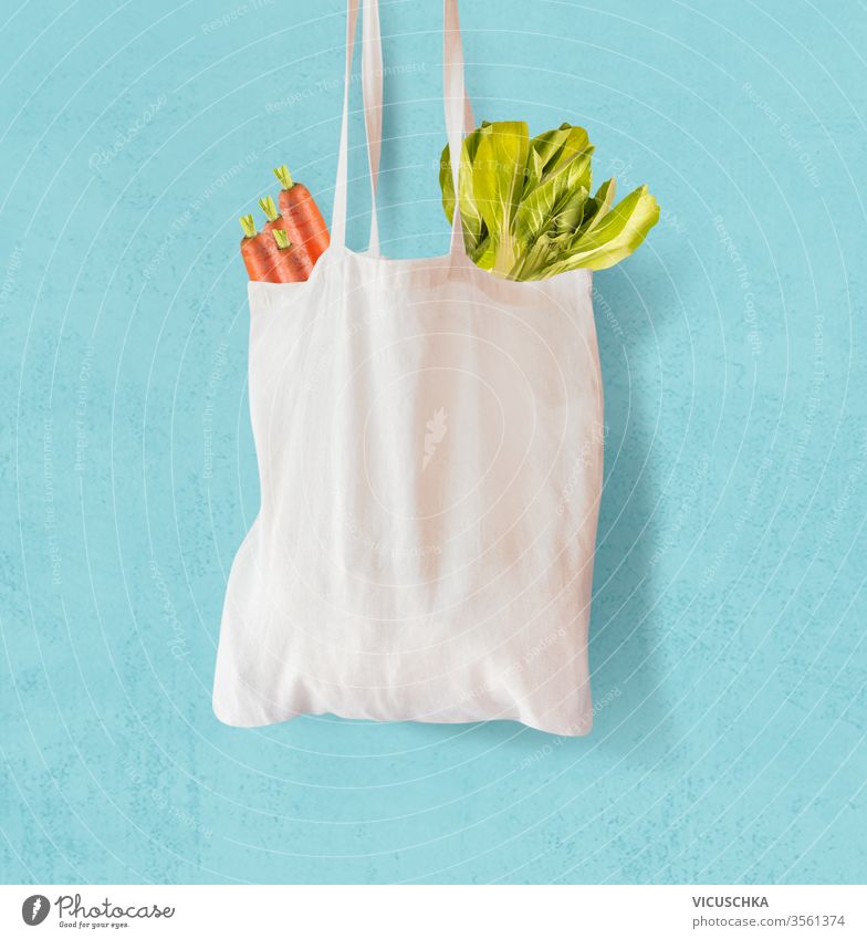 White  textile grocery shopping bag with vegetables hanging at light blue background. Zero waste concept. Cotton reusable bag. Plastic free shopping. Eco friendly bag mock up.
