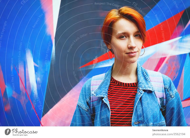 Young adult white woman in jeans jacket with died red hair, lifestyle portrait with selective focus attractive casual caucasian dyed fashion female graffiti