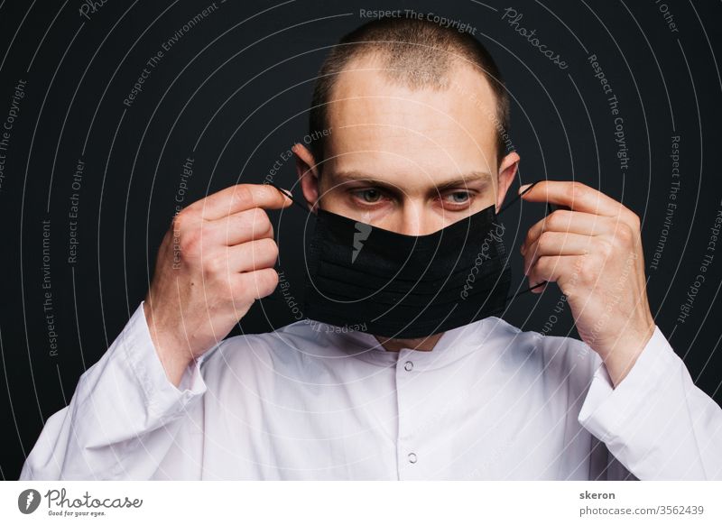 young doctor with short hair in a medical gown uses a black protective mask. male laboratory assistant in a protective suit to work with patients with coronavirus infection during the pandemic.