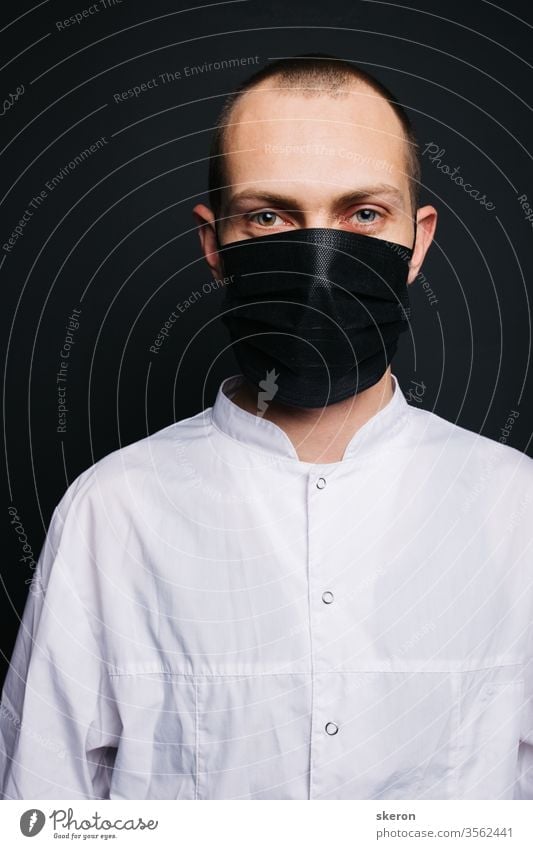 young doctor with short hair in a medical gown uses a black protective mask. male laboratory assistant in a protective suit to work with patients with coronavirus infection during the pandemic.