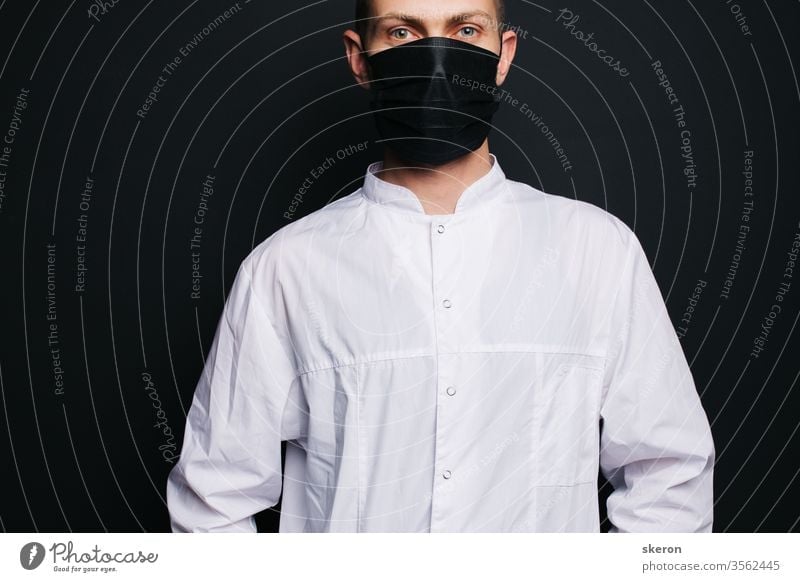 young doctor with short hair in a medical gown uses a black protective mask. male laboratory assistant in a protective suit to work with patients with coronavirus infection during the pandemic.