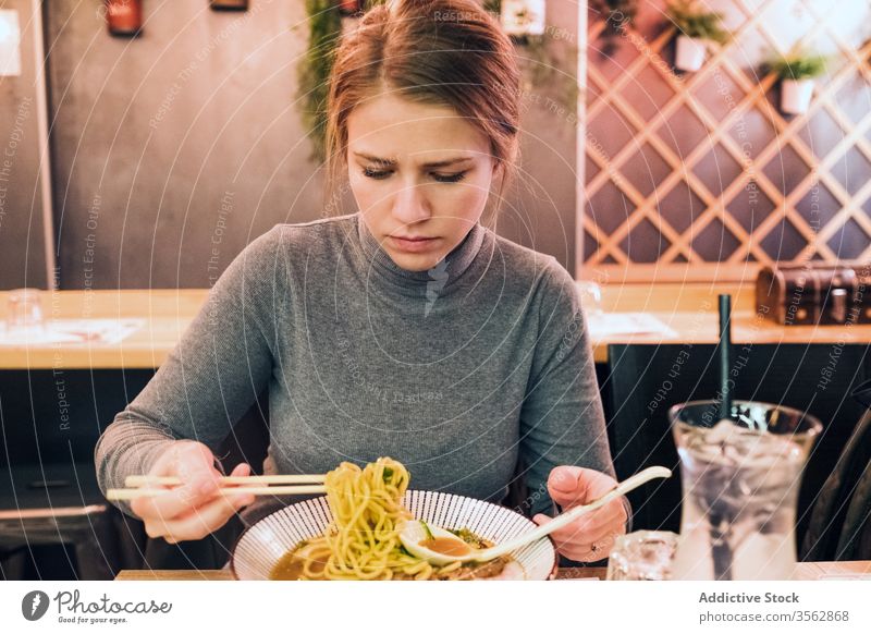 Young woman eating ramen in cafe tradition japanese young spoon chopstick bowl female dish table tasty cuisine lifestyle restaurant food meal delicious asian