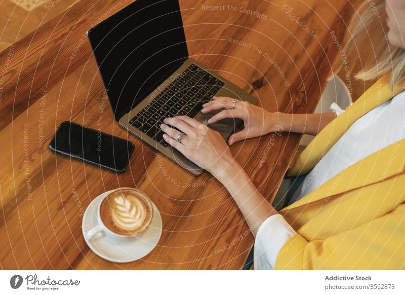 Adult woman drinking aromatic coffee while working on laptop in coffee shop freelance using cafe foam internet latte cup home beverage cappuccino surfing
