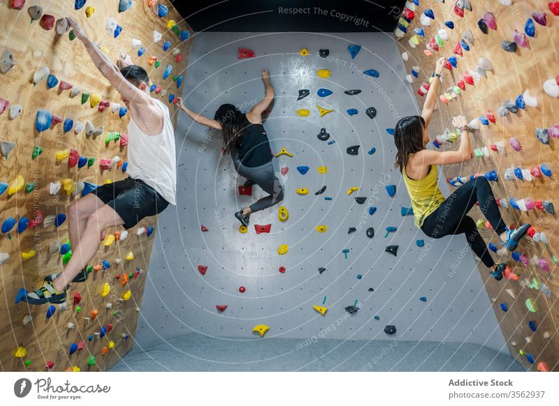 Climbers in sportswear on wall in gym challenge energy man strong power boulder lifestyle group move side view muscular skill courage belay high male horizontal