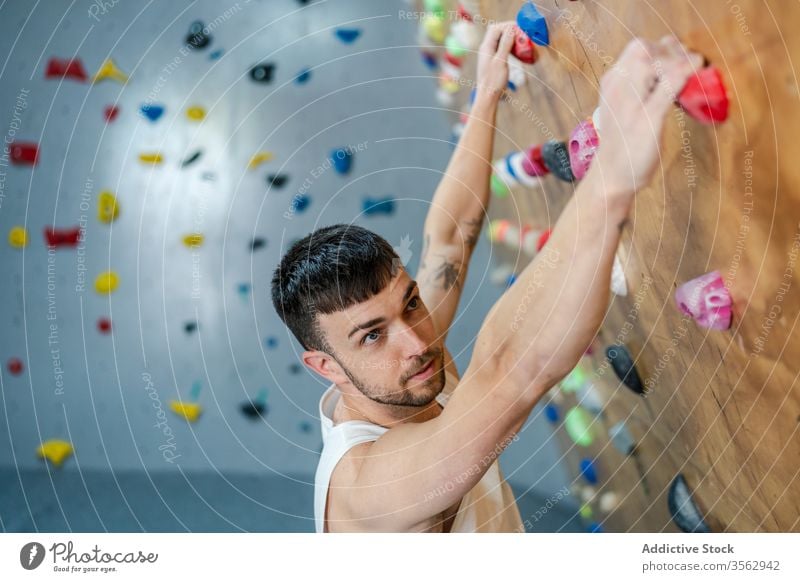 Focused male climber hanging on wall man sport training boulder equipment gym activity workout athlete hobby extreme strong club exercise effort active rock