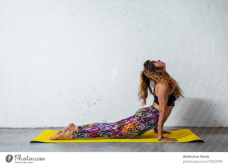 Woman practicing yoga on mat woman practice upward facing dog pose bhujangasana posture position balance eyes closed flexible concrete activity wall modern