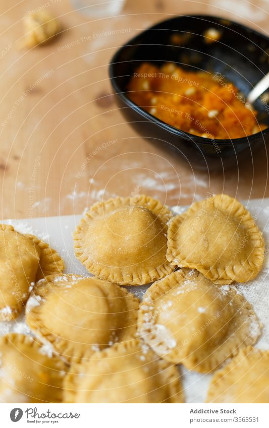 Raw ravioli on table in kitchen cutting board round circle fill pumpkin puree cookery flour raw utensil prepare food italian gastronomy kitchenware bottle tasty