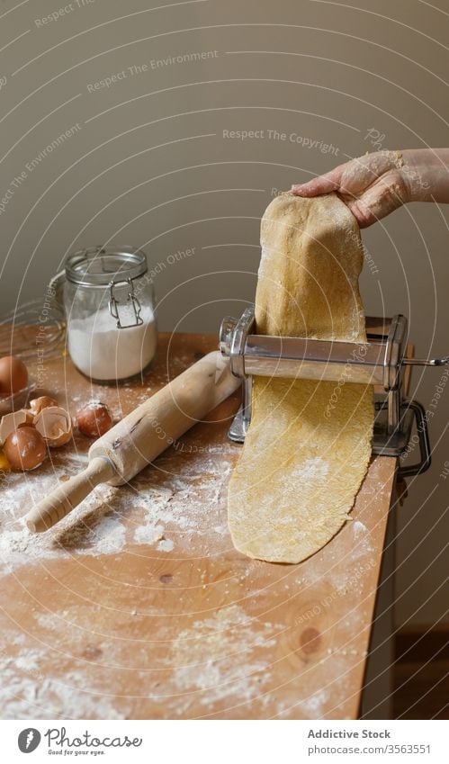 Anonymous female cook rolling dough while using pasta machine woman pastry elastic flour appliance kitchenware egg instrument glass whisk prepare eggshell