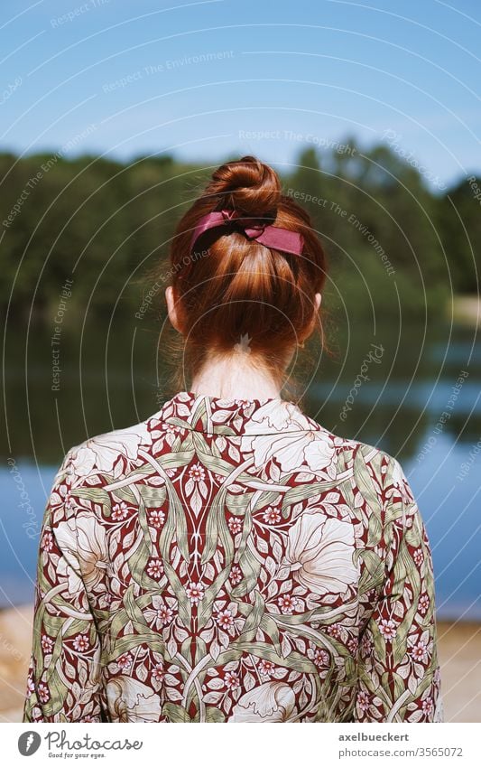 rear view of young woman alone in nature girl back solitude depression messy bun red hair head lake standing floral dress unrecognizable person people women