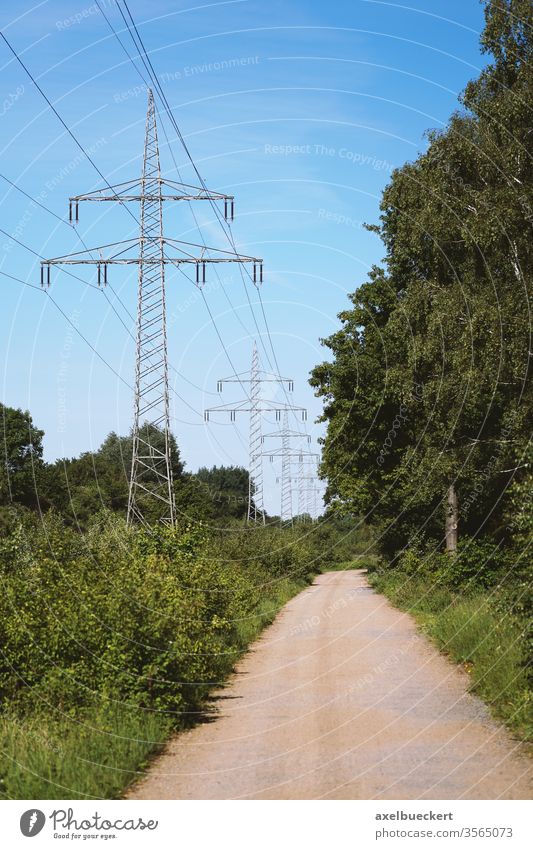 transmission line or overhead power cable along rural dirt track path through countryside high-voltage electricity pole pylon landscape tower nature road