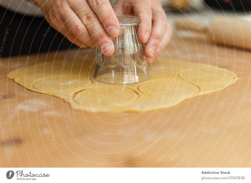 Anonymous male cook using glass for cutting round form for ravioli cutter dough ingredient press rolling pin circle table wooden prepare process man kitchen