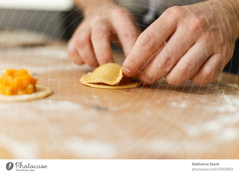 Crop person stuffing ravioli with pumpkin filling dough prepare circle cook table round wooden process kitchen food cuisine culinary homemade dish recipe