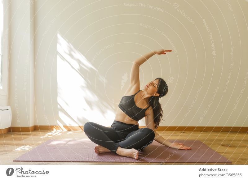 Flexible woman doing side bend and practicing yoga practice exercise flexible mindfulness serene sukhasana living room female stretch home tranquil focus