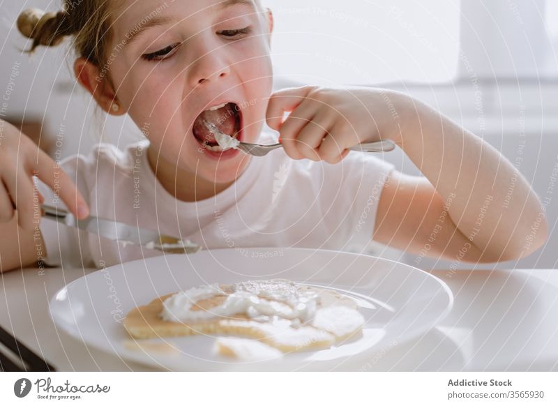 Excited girl having breakfast in kitchen in morning excited child pancake thrill tasty whipped cream adorable kid delicious bright food table sit childhood meal