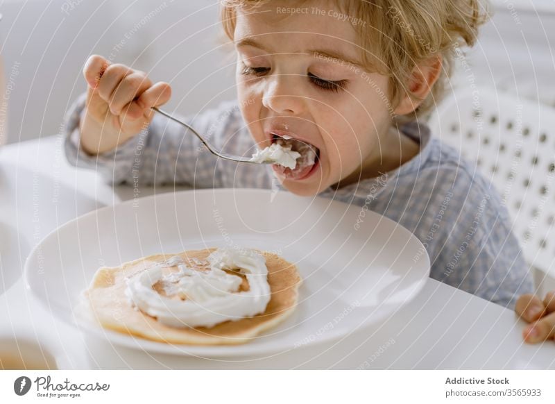 Little child eating pancake with whipped cream kitchen adorable kid delicious breakfast bright food table sit childhood tasty meal home nutrition morning sweet