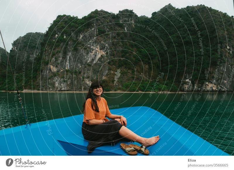 Young woman sitting at the bow of a boat and laughing into the camera. Halong Bay in Vietnam. Woman Laughter vacation travel ship Trip Tourist Attraction