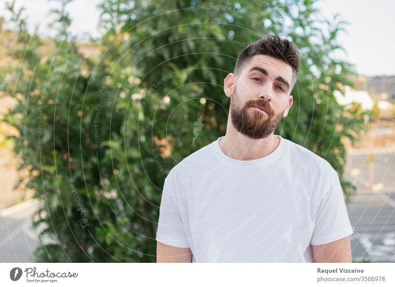 Handsome man with a beard and white t-shirt outdoors. portrait young handsome happy smiling person people park smile casual guy face men outside green boy one